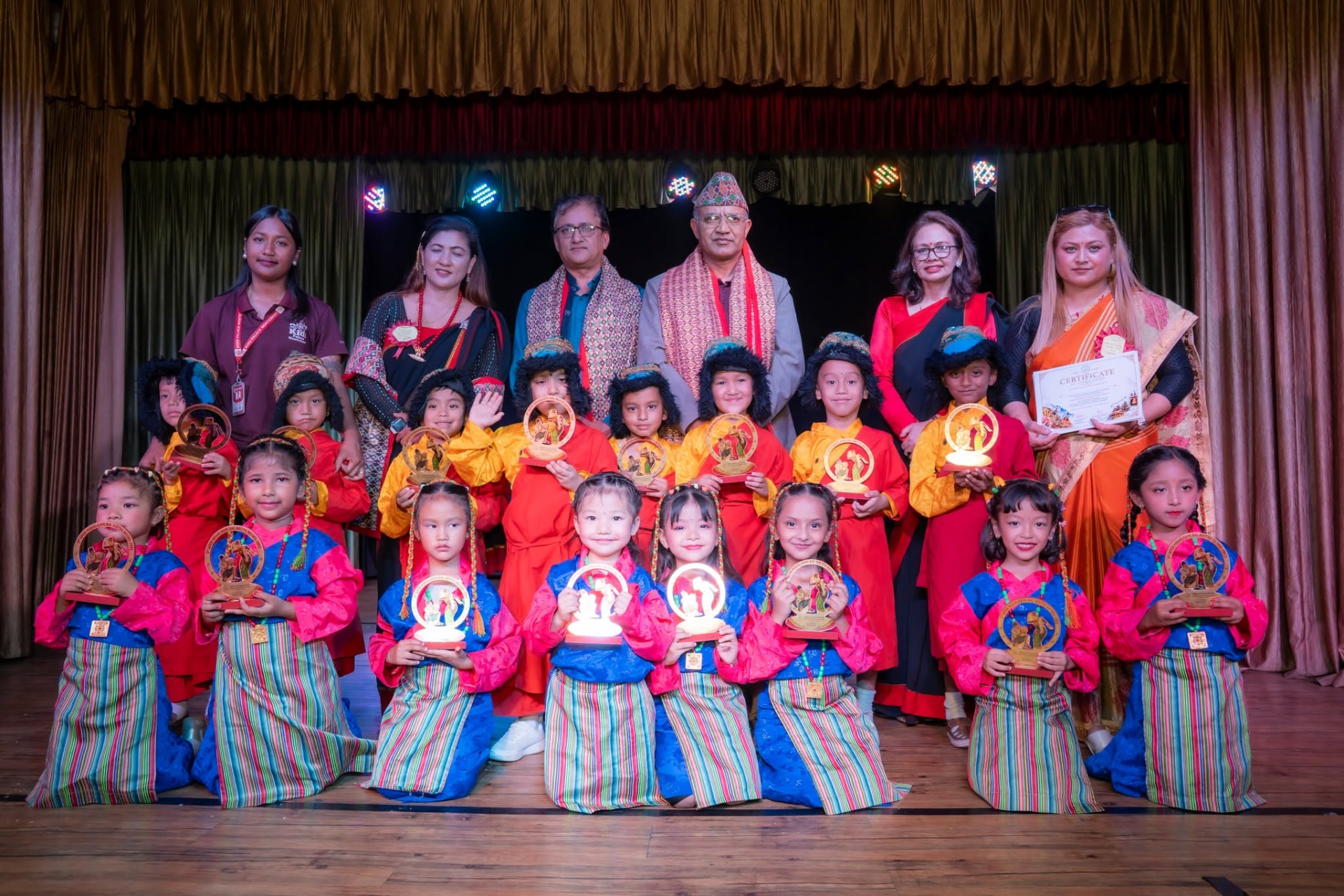 Heimric dancers holding their trophies on stage with teachers and guests after a cultural competition
