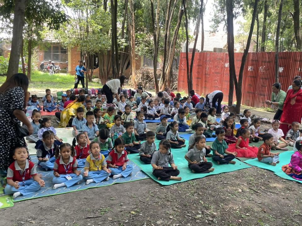 Students sitting cross-legged on mats for an outdoor meditation session under the trees