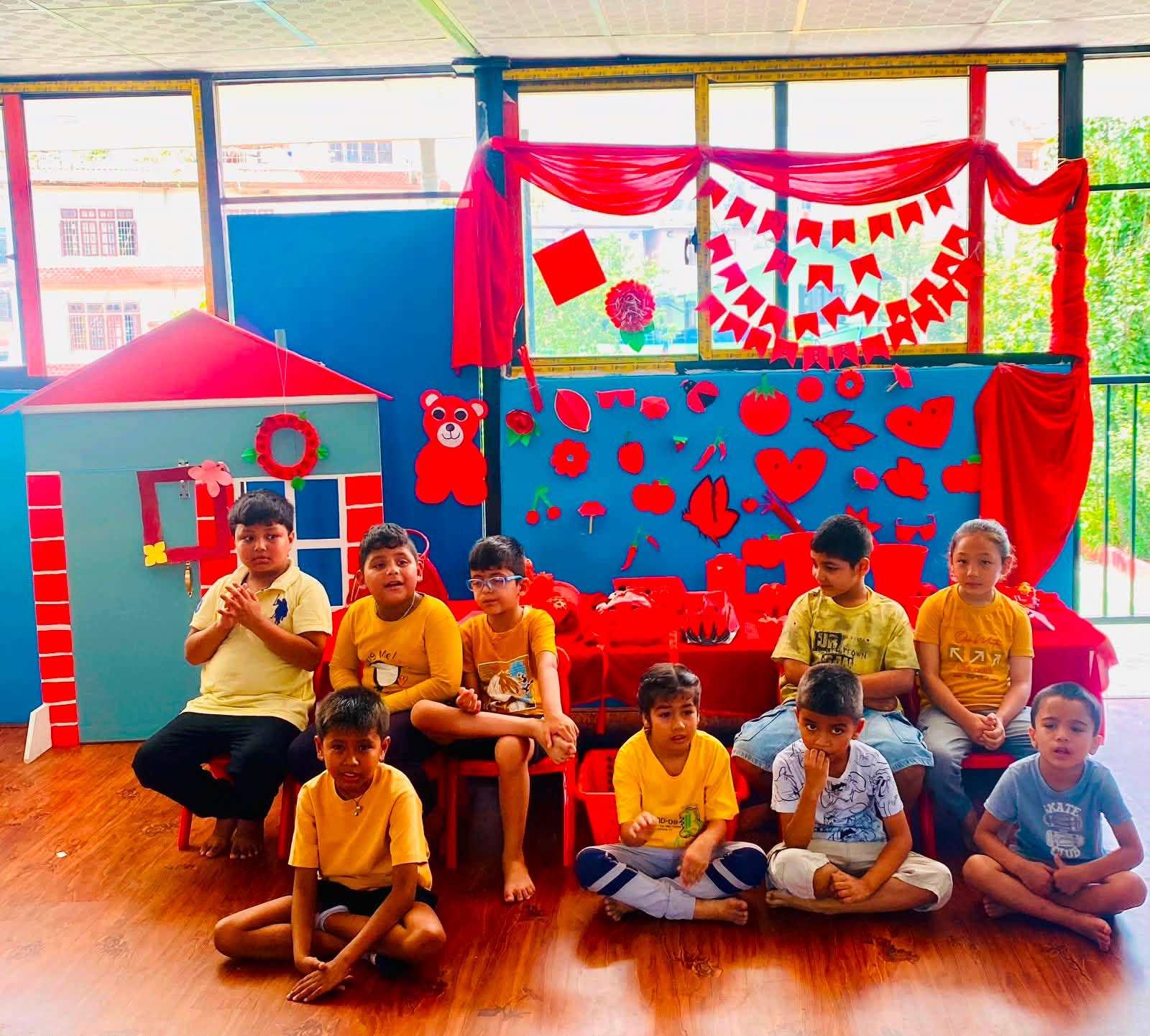 Children in yellow tees in front of the classroom Red Colour Day display of handmade red objects