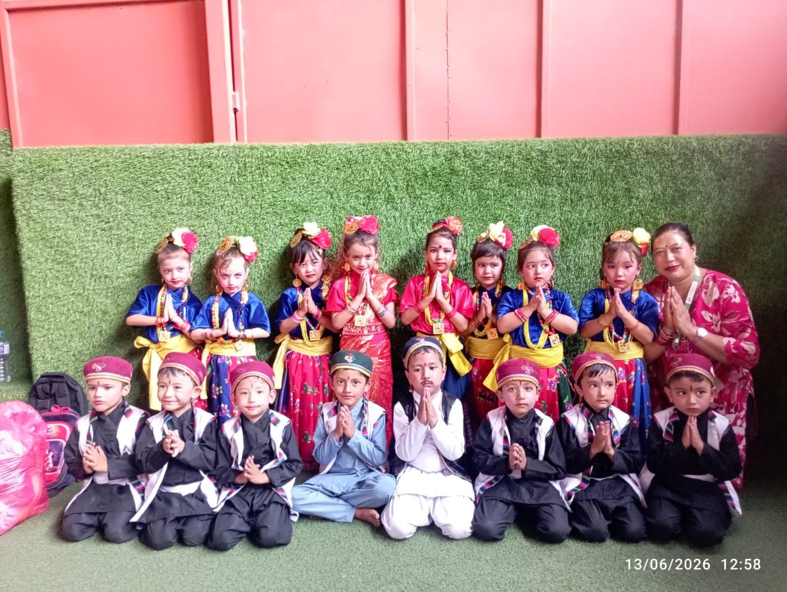 Young students in traditional Nepali dress greeting with folded hands beside their teacher