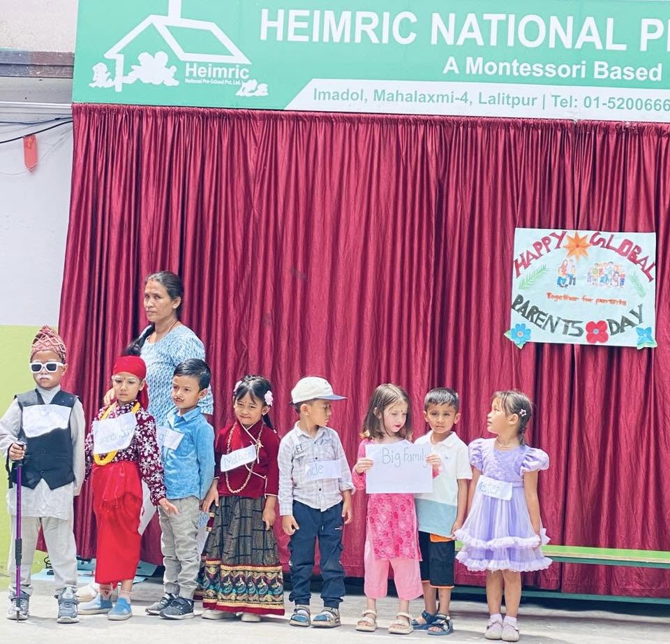 Children in colourful costumes on stage under the Heimric Parents Day banner
